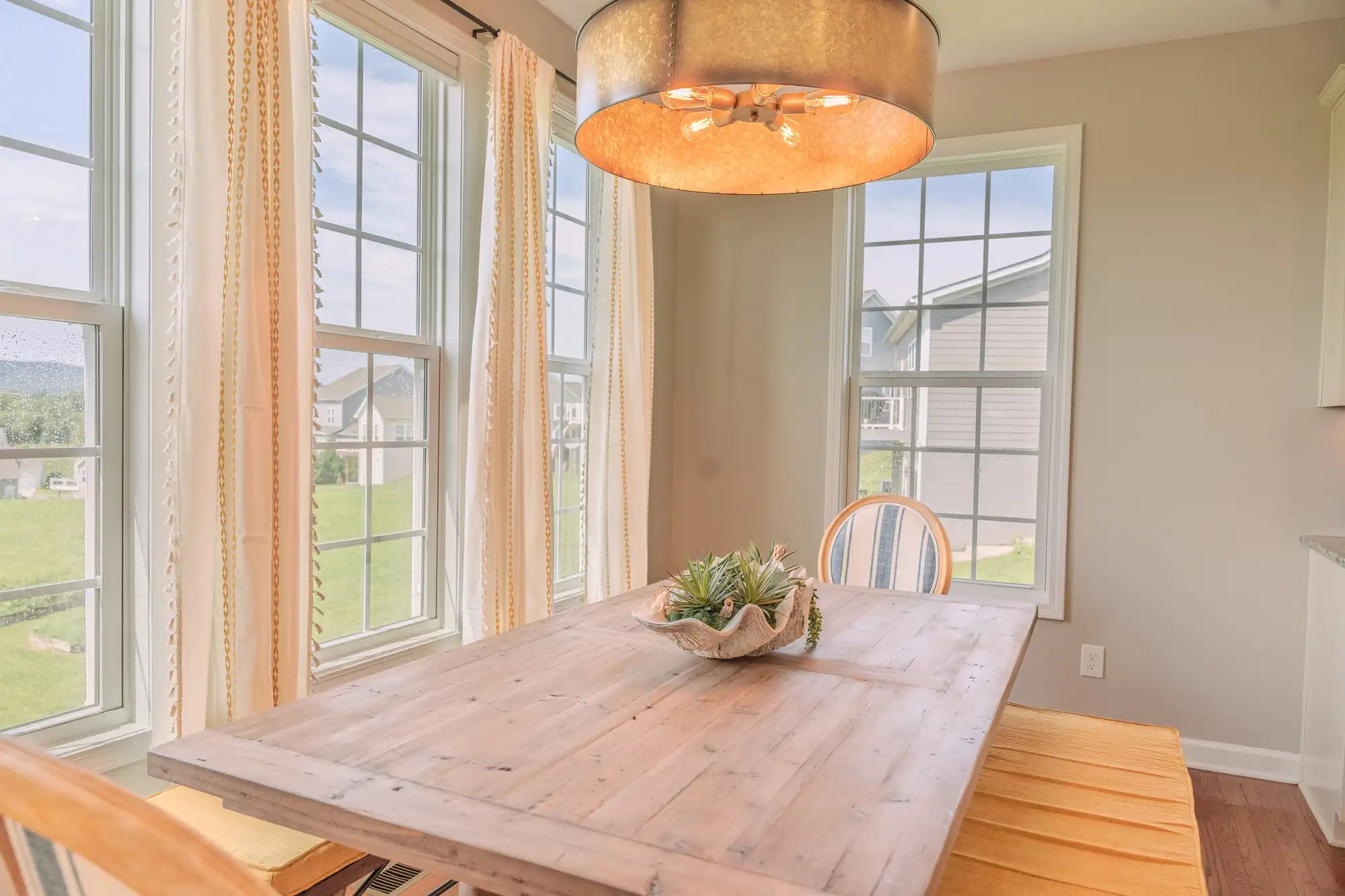 Wood breakfast table and bench beneath a warm pendant light beside tall windows