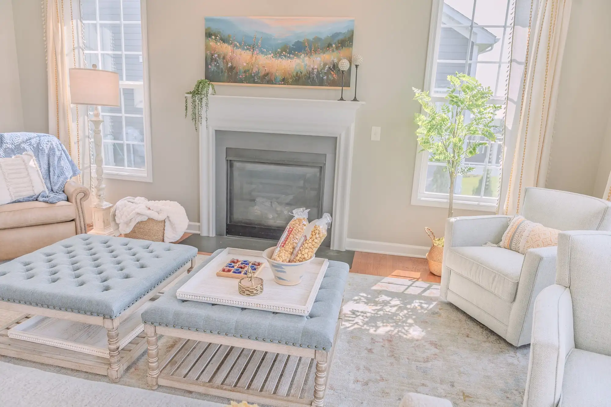 Fireplace beneath a landscape painting, framed by windows and soft blue seating