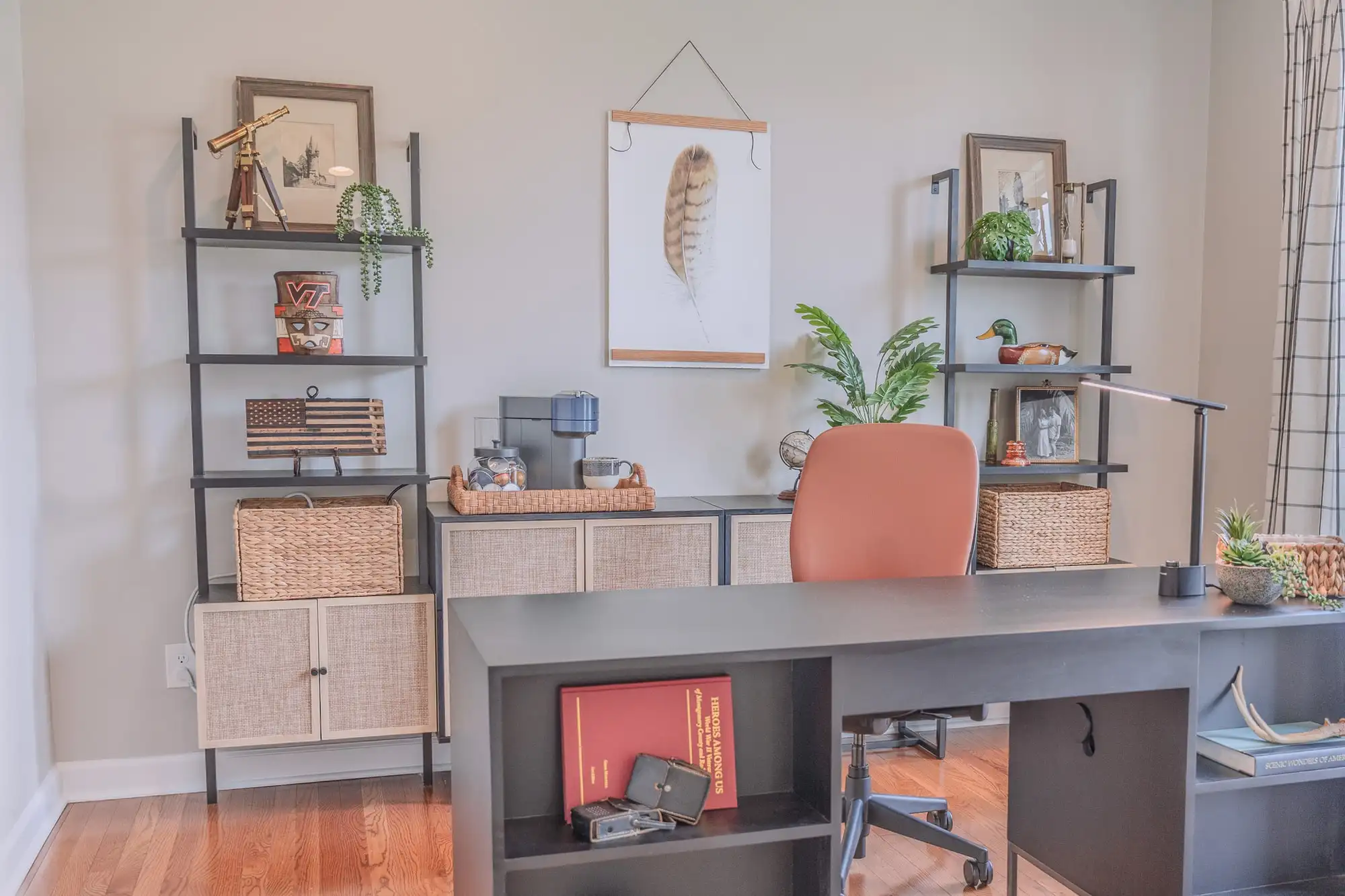 Home office with a dark desk, rust-colored chair, open shelving, and framed feather art