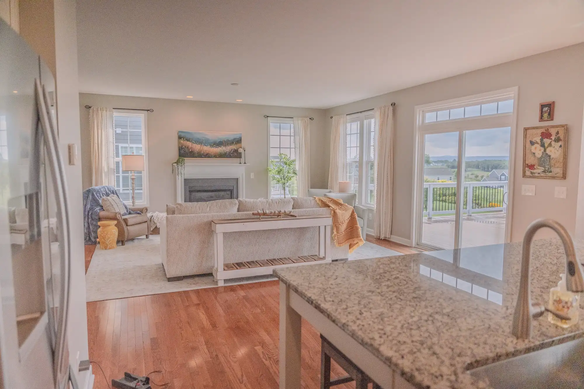 View across a stone kitchen counter toward the sofa, fireplace, and tall living room windows