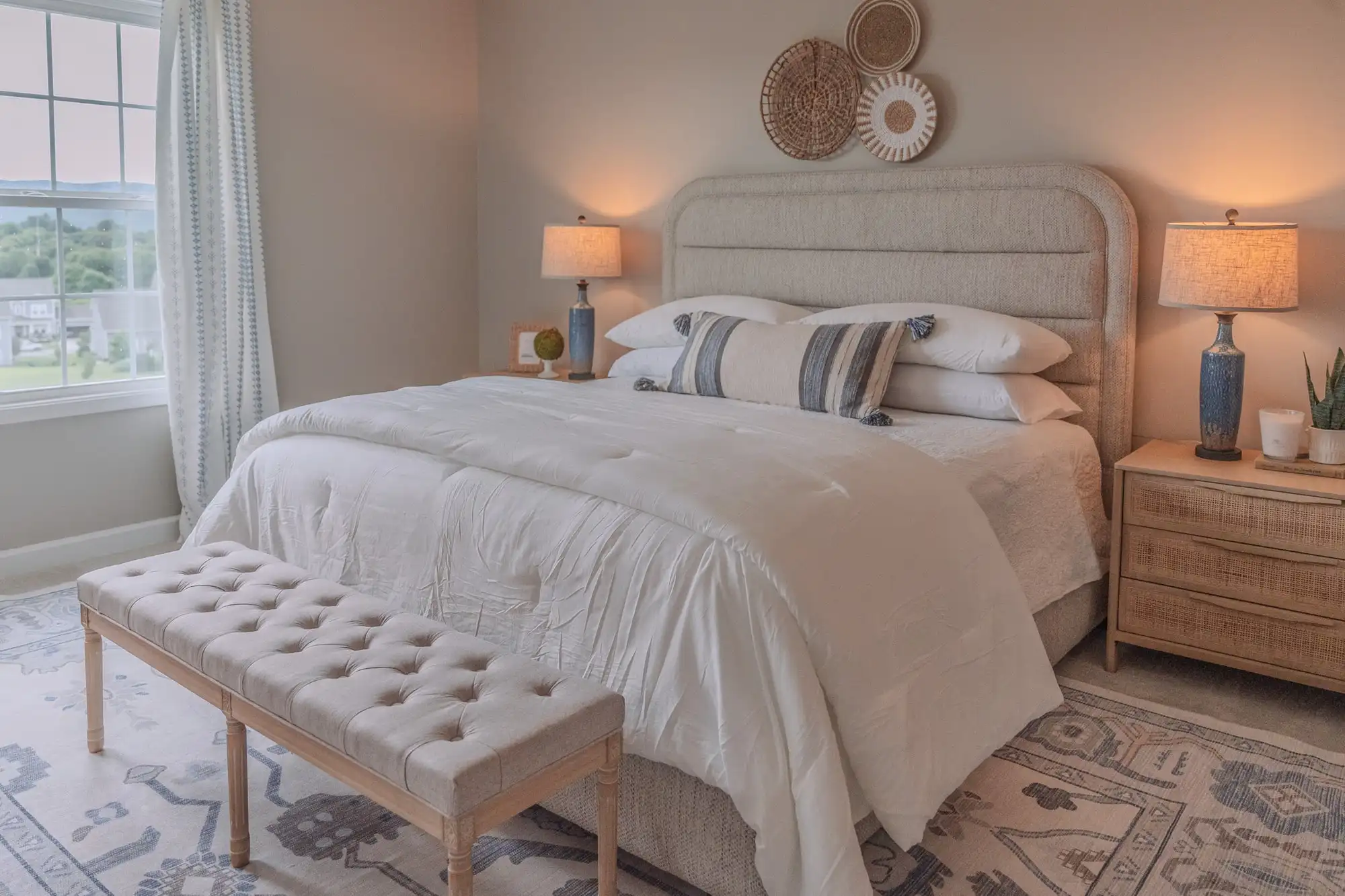 Bedroom with an upholstered headboard, white bedding, blue lamps, and a tufted bench