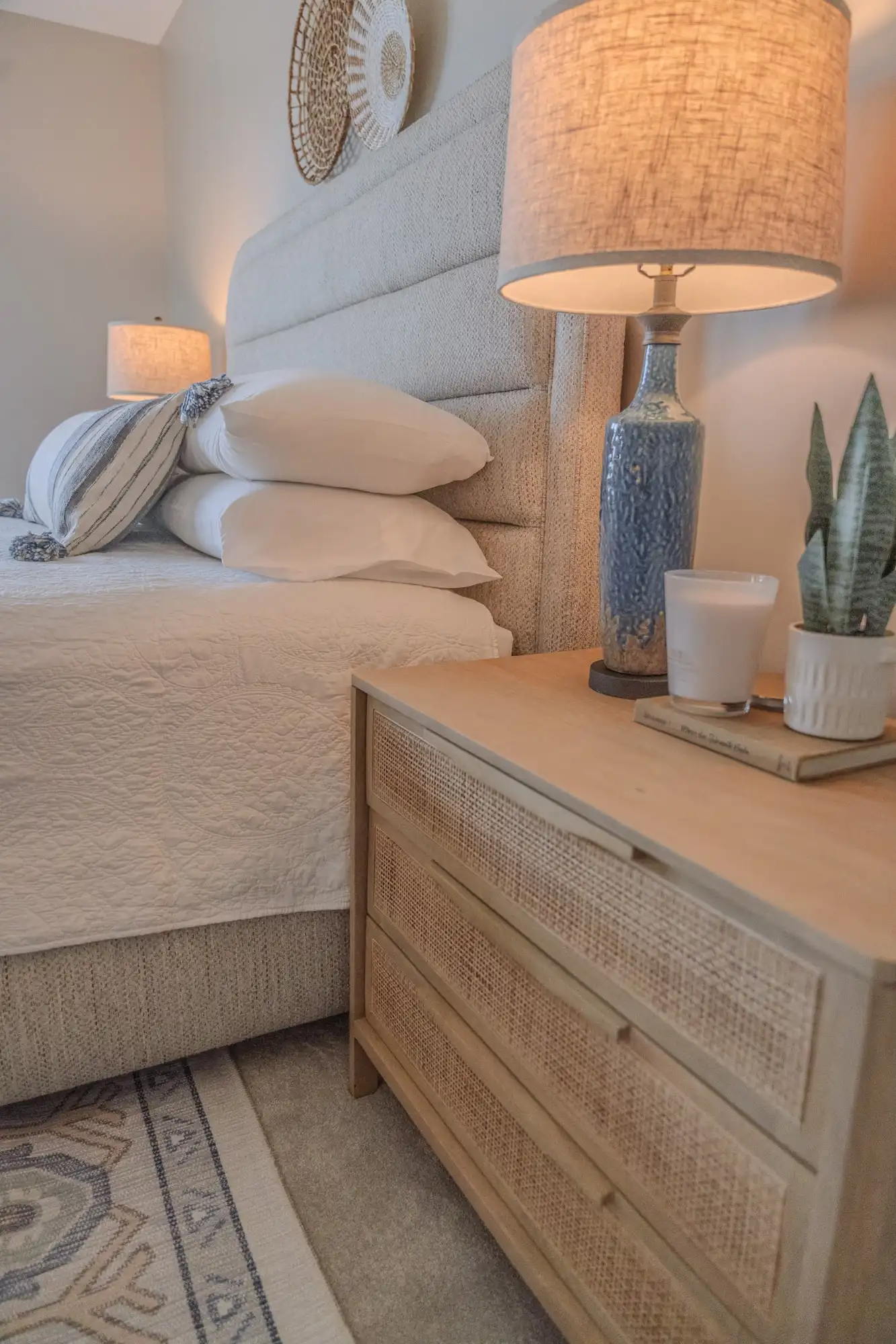 Blue bedside lamp and plant on a wood nightstand beside an upholstered headboard