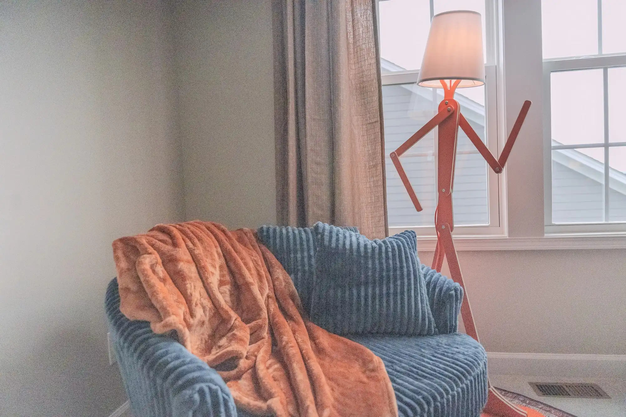 Blue corduroy chair with an orange throw beside a red figure-shaped floor lamp