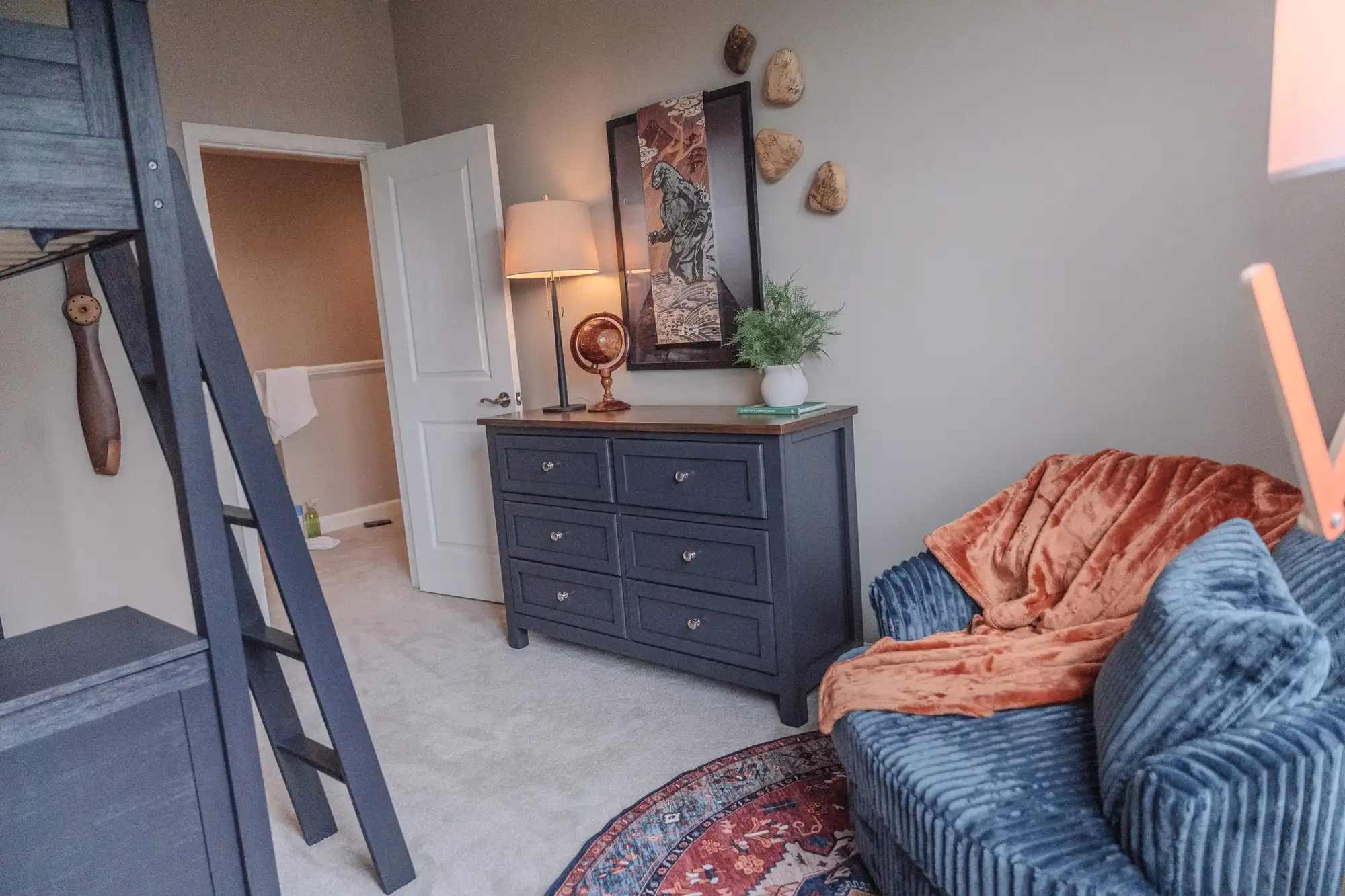 Bedroom with a dark loft bed, dresser, blue chair, and orange throw