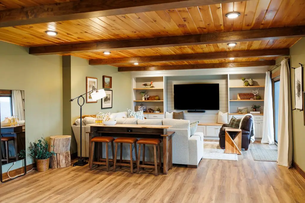 Living room with exposed timber ceiling, pale sectional, and a dark console with leather-topped stools