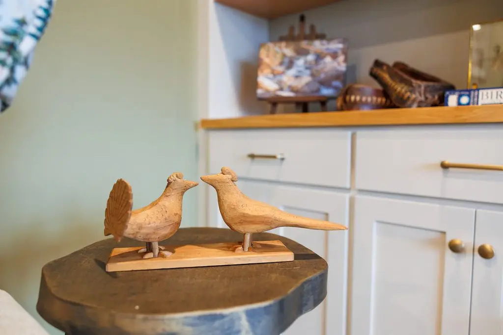 Two carved wooden birds on a stump side table beside styled built-in shelving