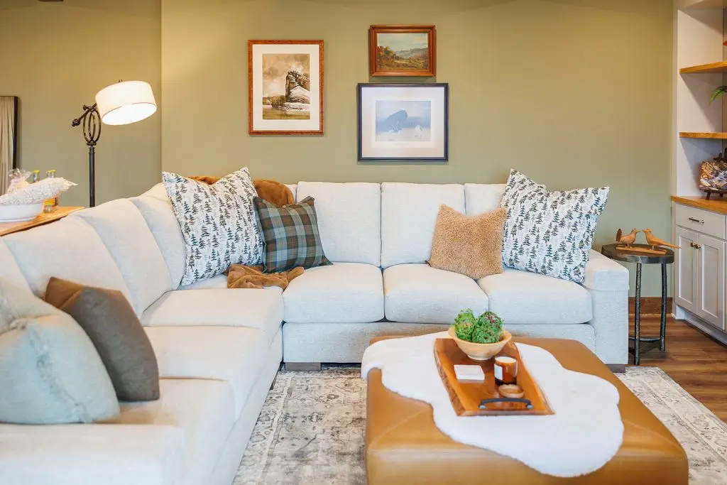 Pale sectional layered with blue patterned cushions against a green wall with framed art