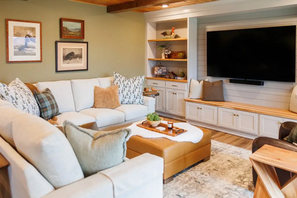 Sectional sofa and tan ottoman facing built-in shelves in a soft green living room