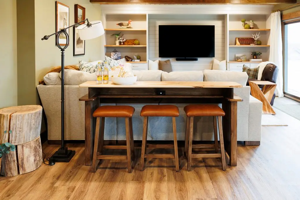 Wood console and three leather-topped stools behind a pale sectional beneath a timber ceiling