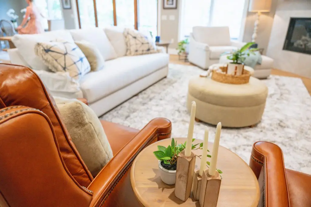 Cognac leather armchair beside a sofa with blue patterned cushions and a round upholstered ottoman