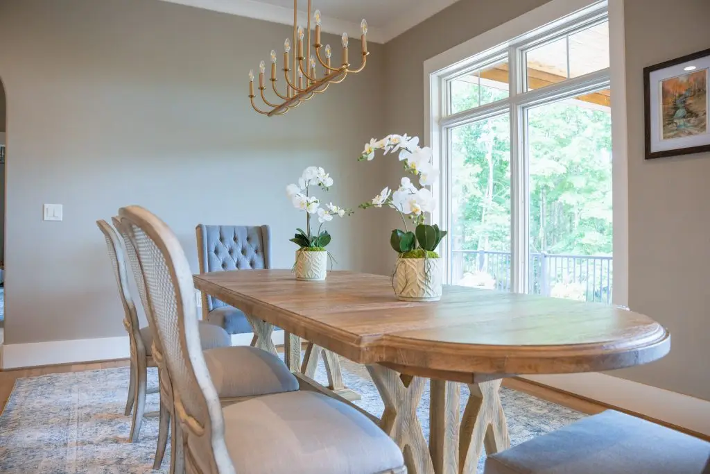 Wood dining table with upholstered chairs, white orchids, and a brass chandelier
