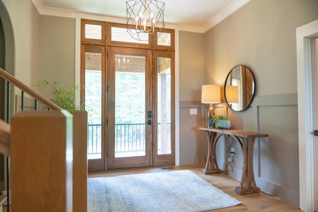 Entry with a wood-framed glass door, round mirror, and curved console table