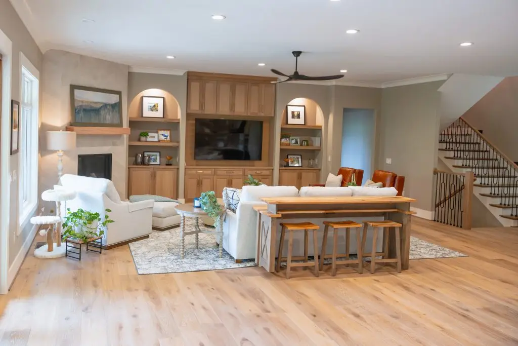 Open living room with wood built-ins, pale seating, and a console with stools behind the sofa