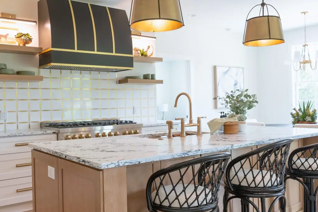 Kitchen with a wood island, woven stools, brass fixtures, and a dark range hood