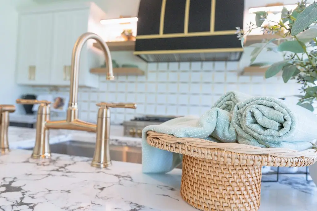 Soft blue towels in a woven basket beside a brass kitchen faucet
